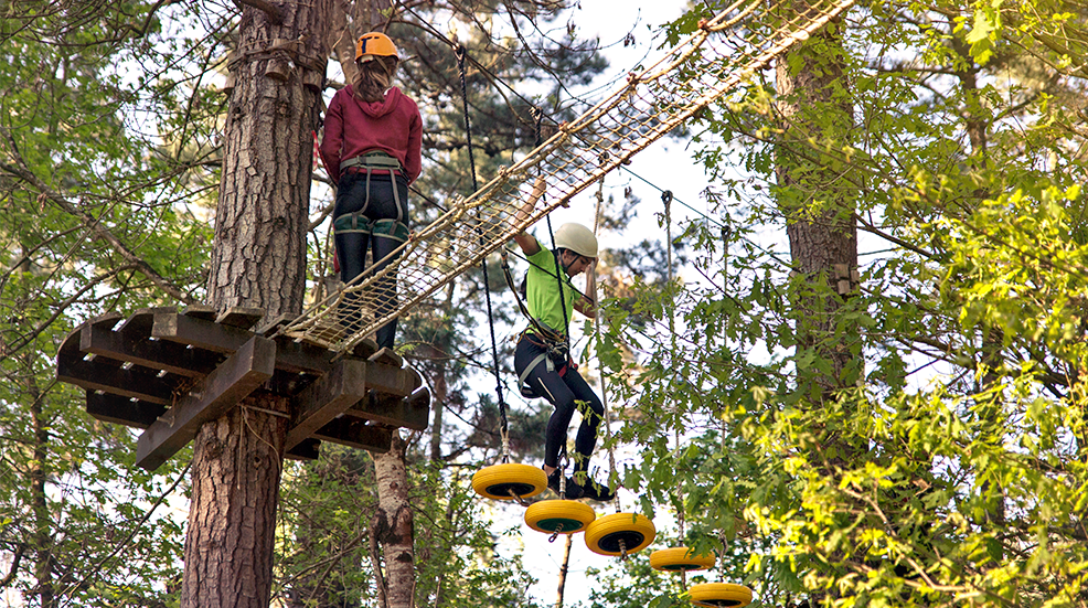 Sisters taking turns climbing and passing obstacles in a multi-adventure park